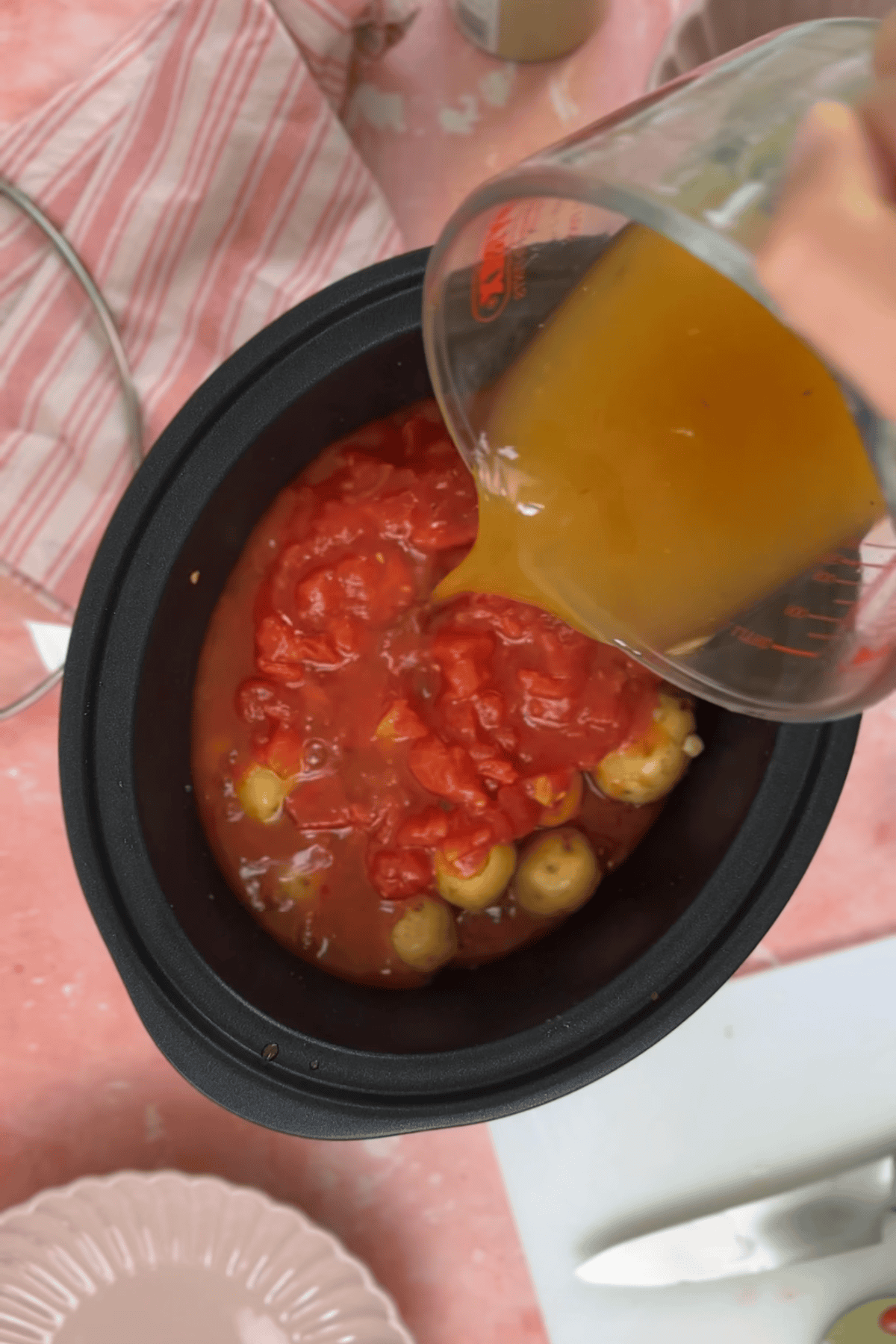 Adding the Greek potato stew ingredients to the slow cooker.