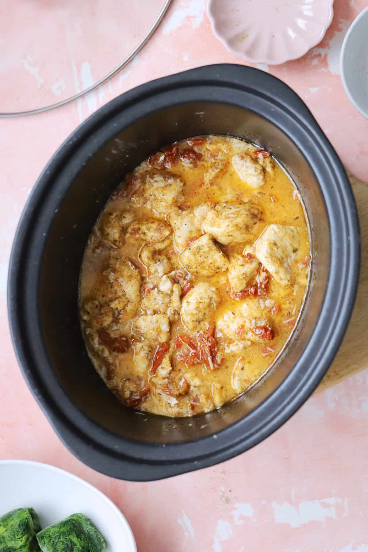 Process shot of slow cooker tuscan chicken recipe showing the chicken, stock, parmesan and tomatoes in the slow cooker.
