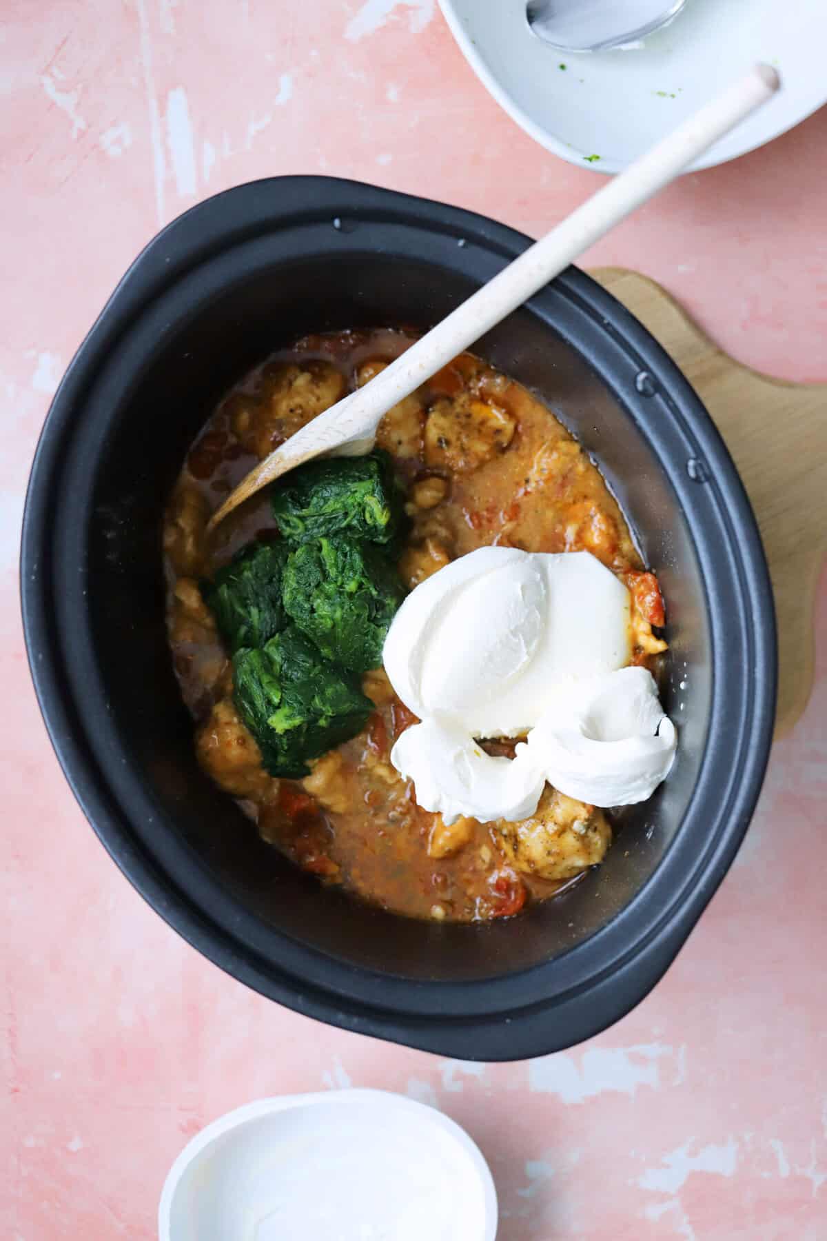Process shot of slow cooker tuscan chicken recipe showing the cream cheese and spinach added to the sauce.