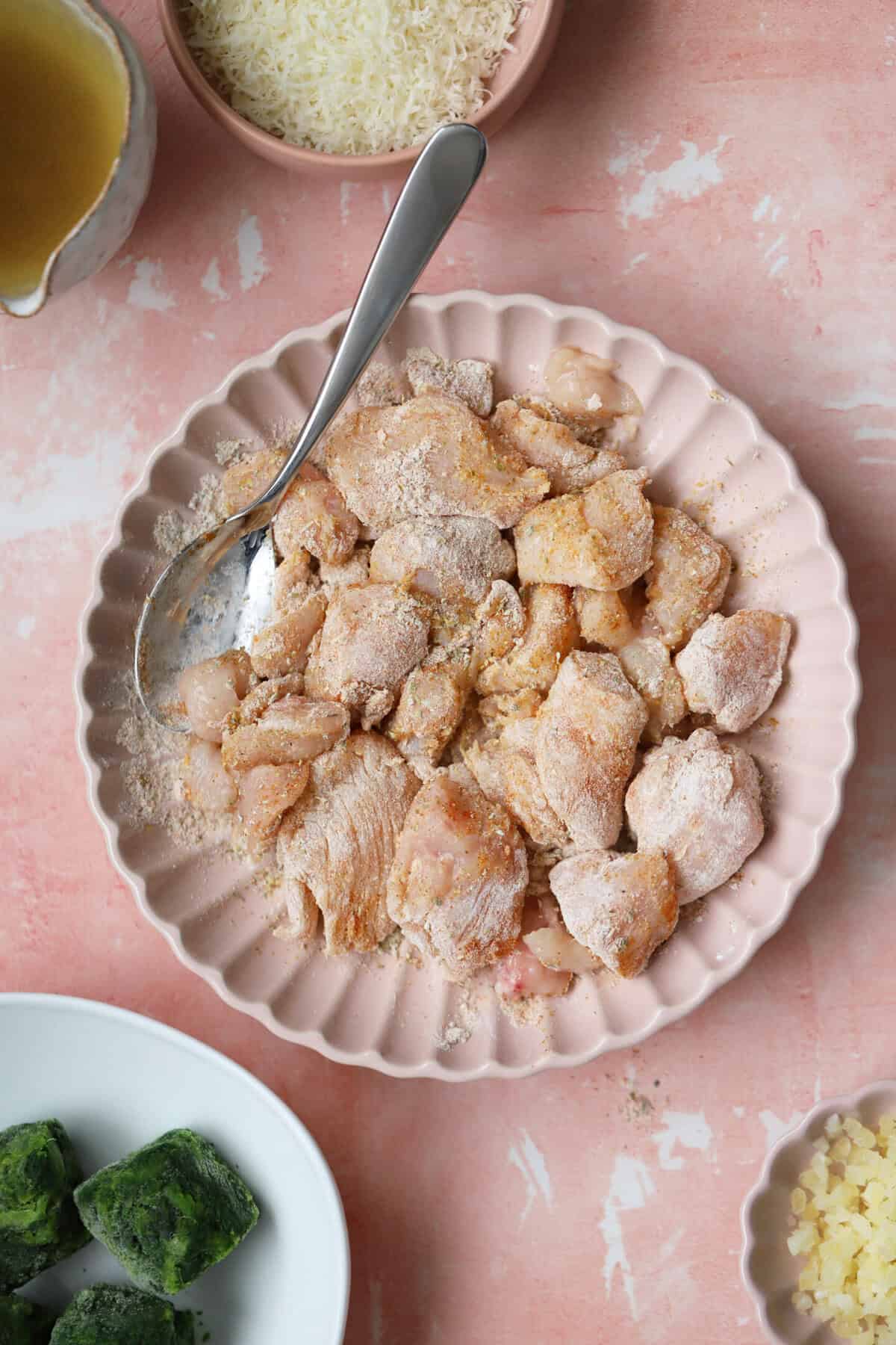 Process shot showing the chicken coated in flour and spices in a bowl.