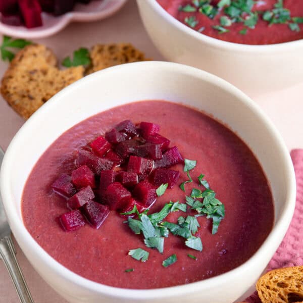A bowl of beetroot soup with brown bread slices behind.