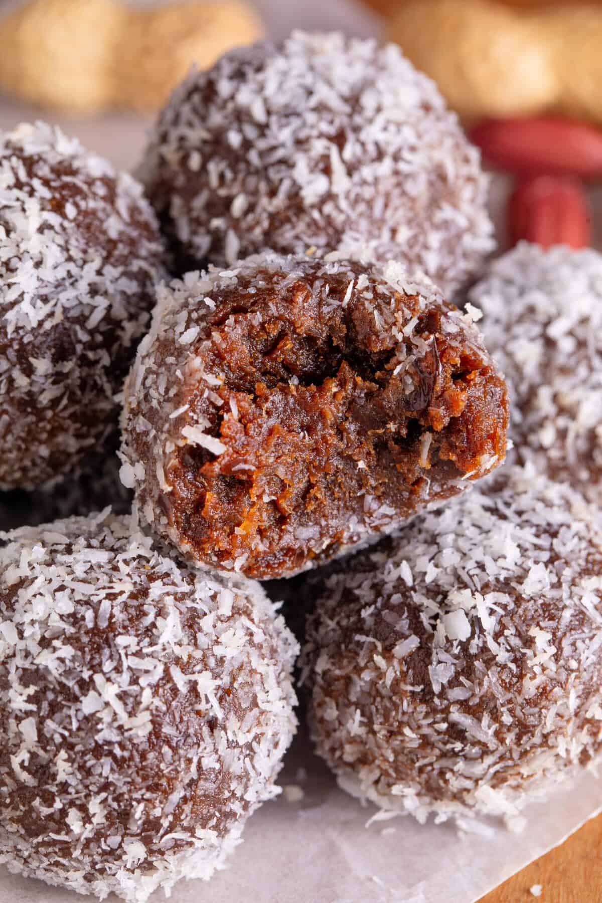 A pile of date energy balls coated in coconut, with a bite taken out of one.