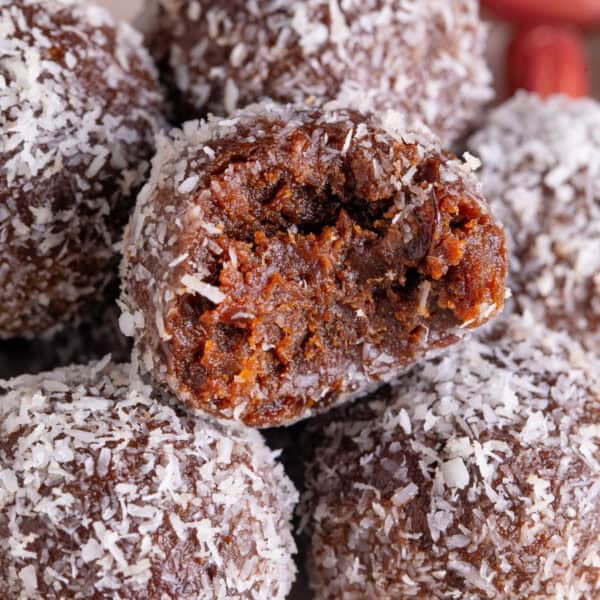 A pile of date energy balls coated in coconut, with a bite taken out of one.