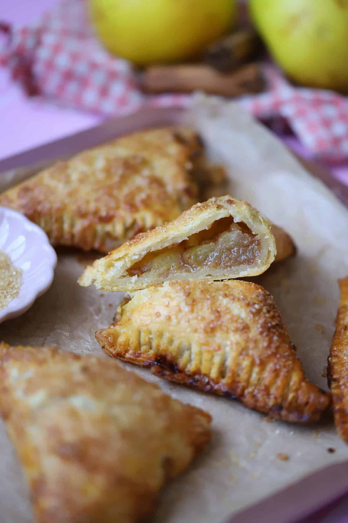 A gluten free apple turnover cut in half on a tray of apple turnovers.