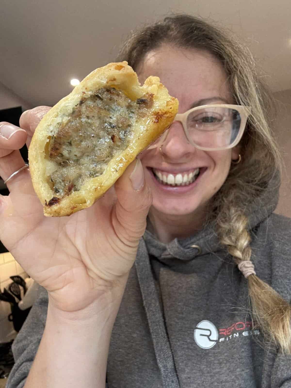 Author Sarah Howells holding up a gluten free sausage roll and smiling.
