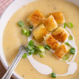A bowl of leek and potato soup with gluten free croutons and a swirl of cream.