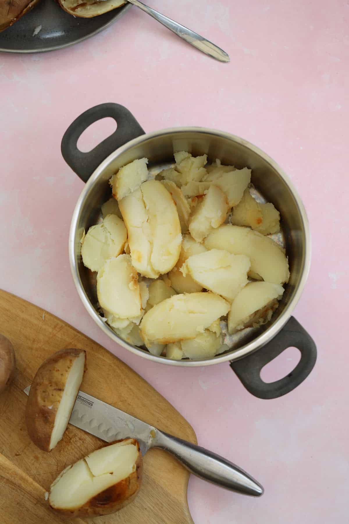 Baked potatoes, with the skins removed, in a saucepan.