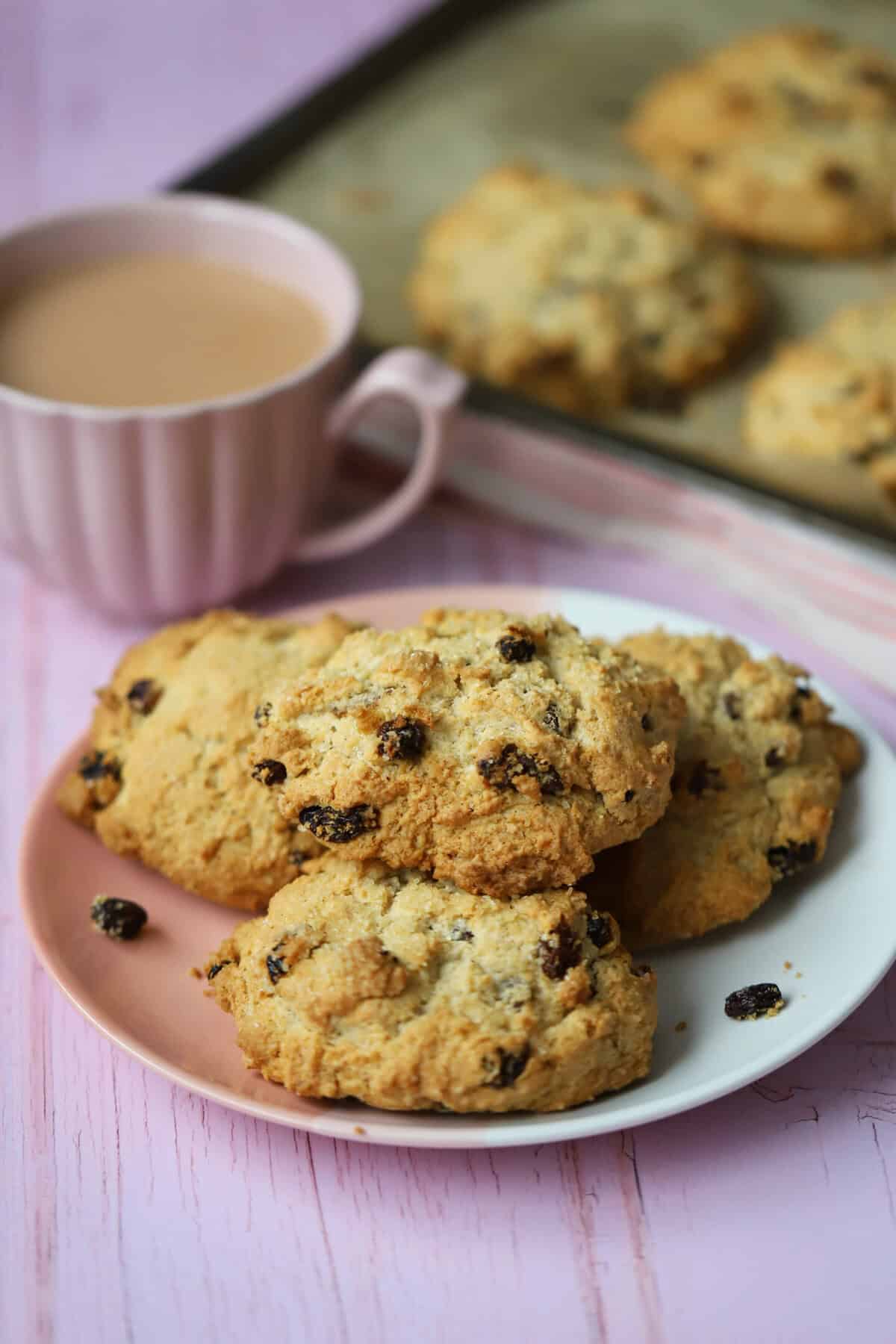 A plate of gluten free rock cakes with a cup of tea behind.