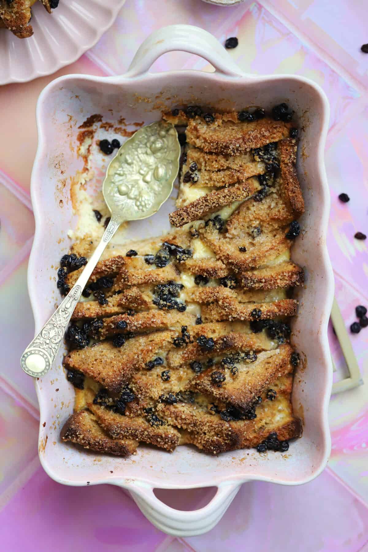 Gluten free bread and butter pudding in a pink dish, with a portion removed and a spoon on top.
