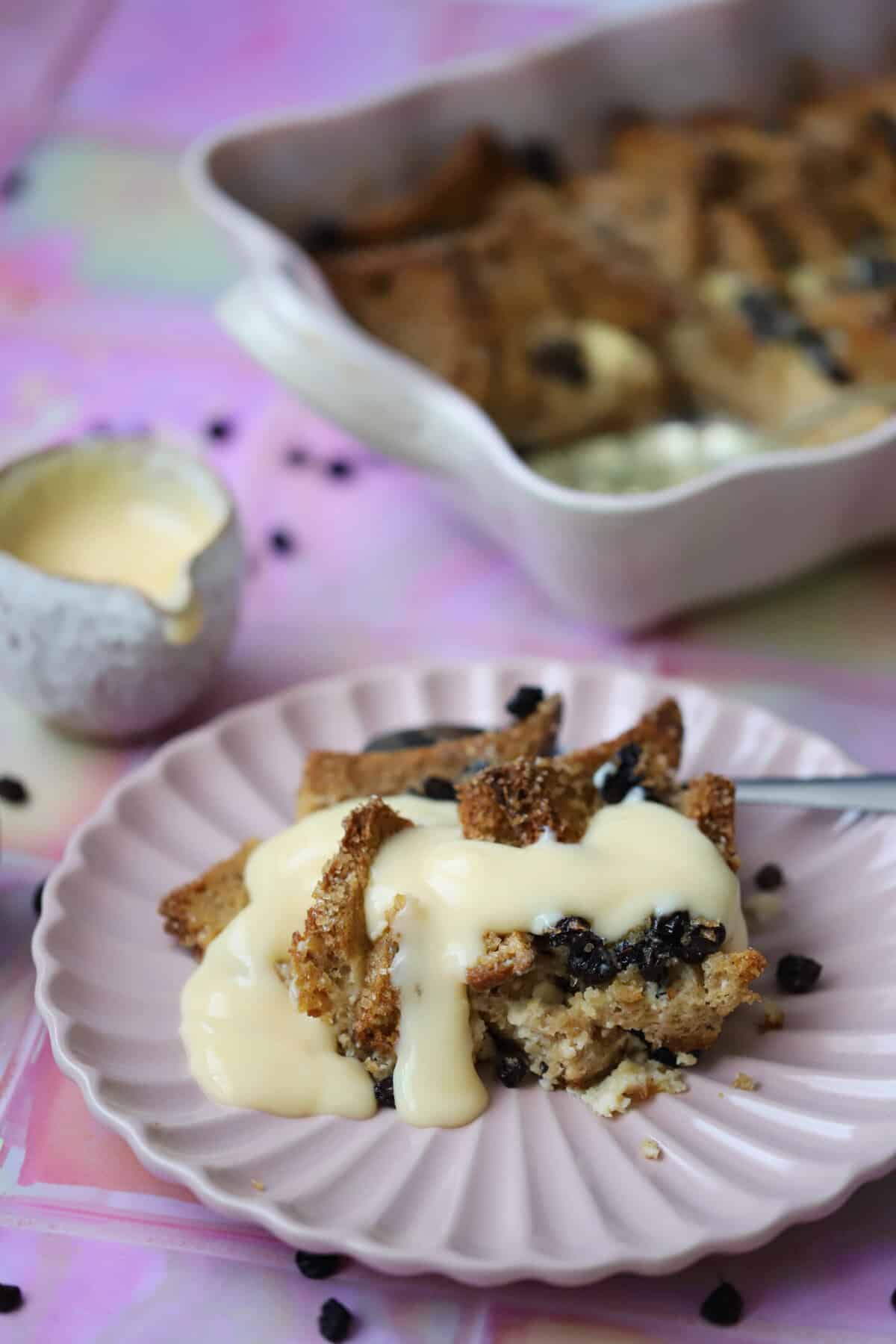 A slice of gluten free bread and butter pudding on a plate with custard.