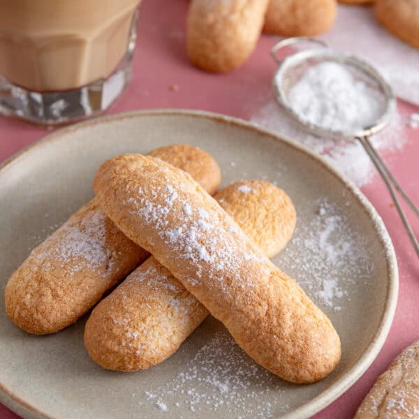 A plate of gluten free ladyfingers with a coffee behind.