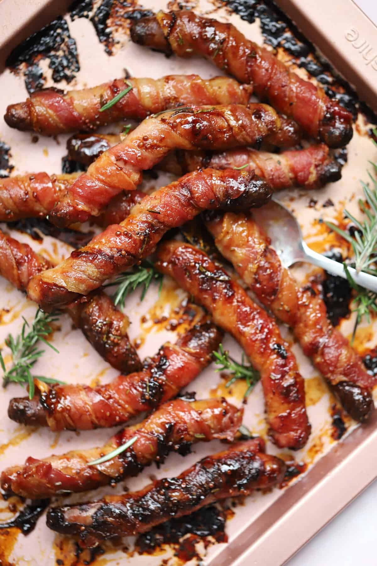 A tray of gluten free pigs in blankets with sprigs of rosemary.