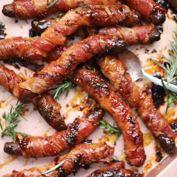 A tray of gluten free pigs in blankets with sprigs of rosemary.