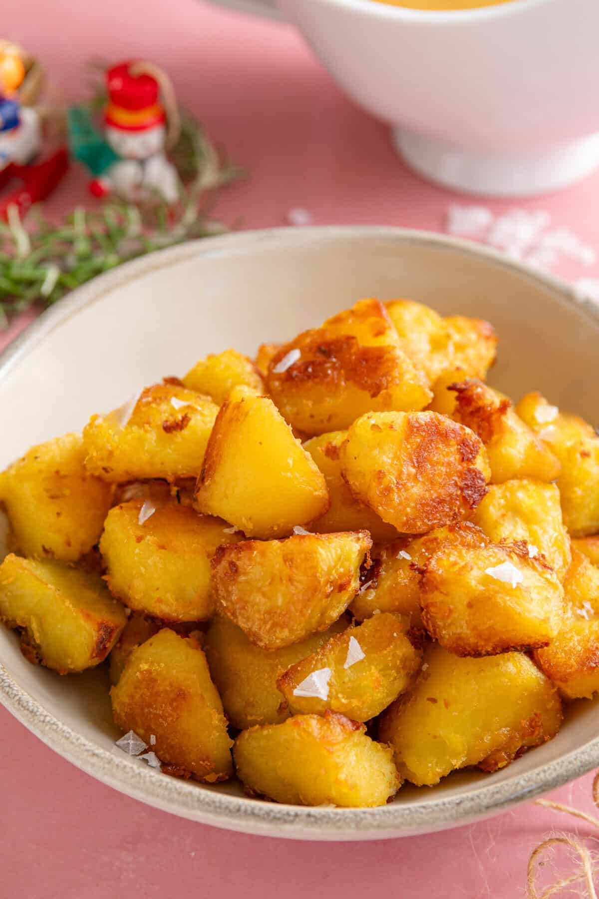 A bowl of crispy roast potatoes with a sprinkle of sea salt flakes on top.