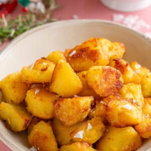 A bowl of crispy roast potatoes with a sprinkle of sea salt flakes on top.