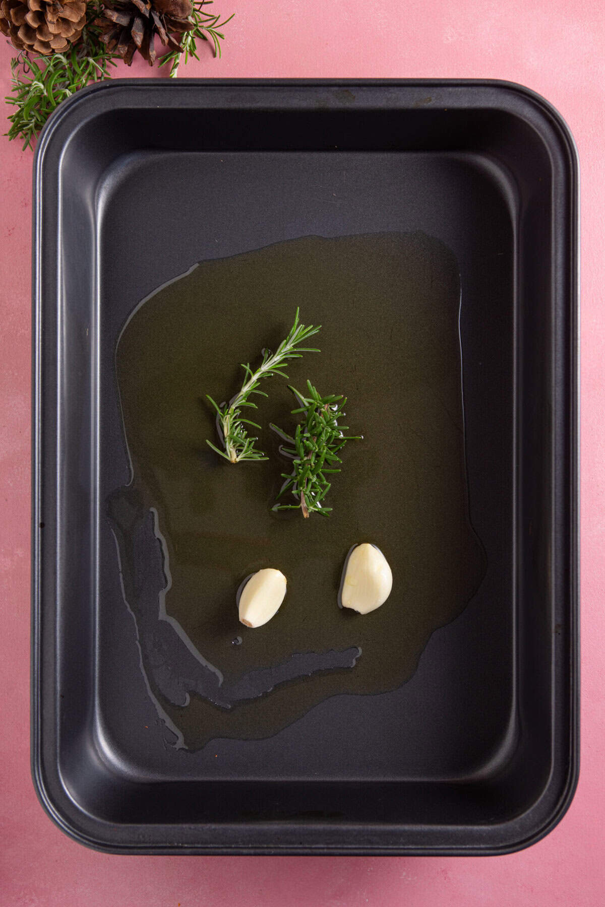 Add the oil, garlic and rosemary to a roasting tin and get it nice and hot in the oven.