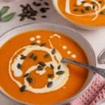 A bowl of roasted pumpkin soup with swirls of cream and pumpkin seeds on top.