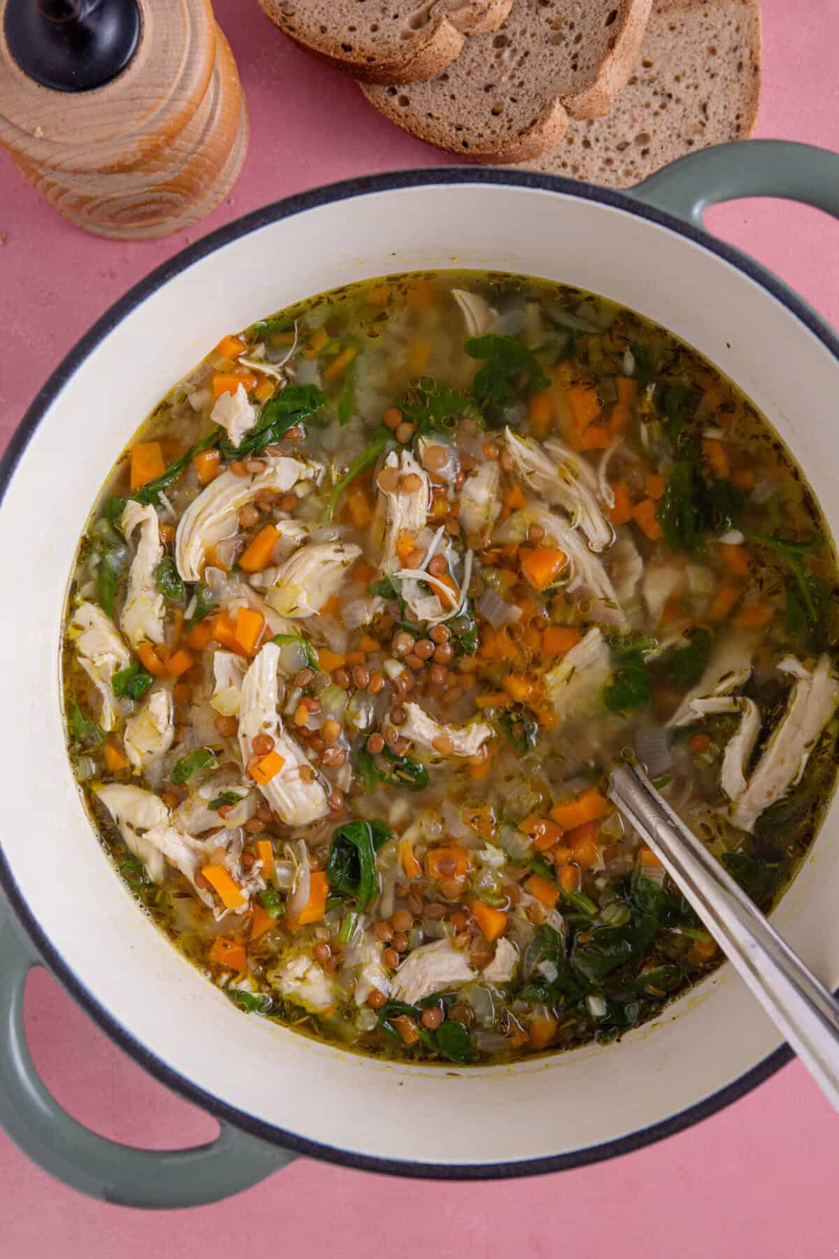 A pan of chicken and lentil soup with a side of gluten free bread.