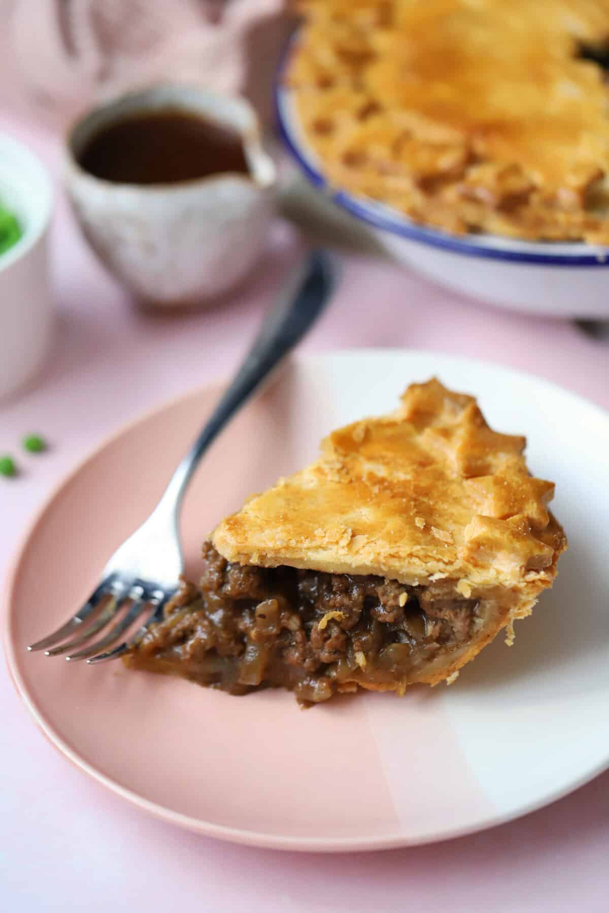 A slice of minced beef and onion pie on a plate showing the rich beef and gravy filling.