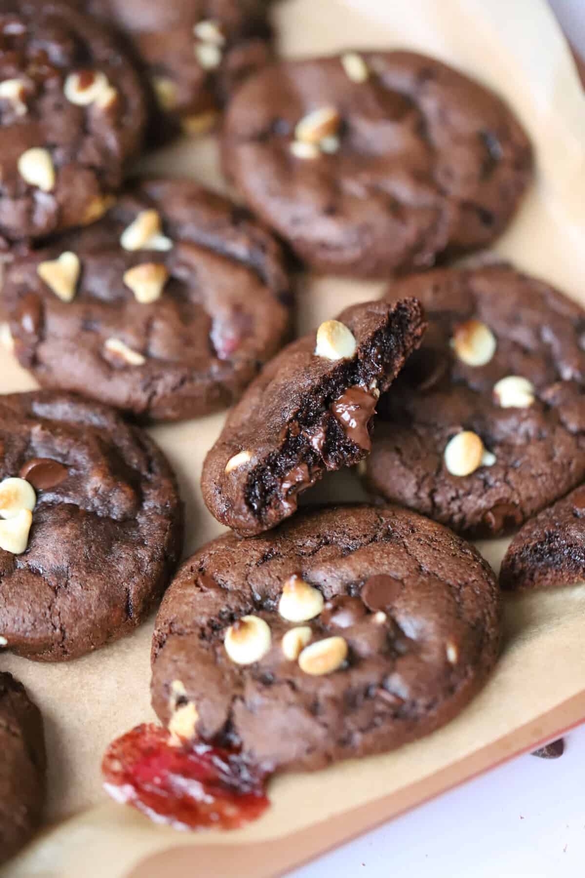 A pile of gluten free peppermint bark cookies - gooey chocolate mint cookies with chunks of white and dark chocolate, with one cut in half to show the gooey chocolate inside.