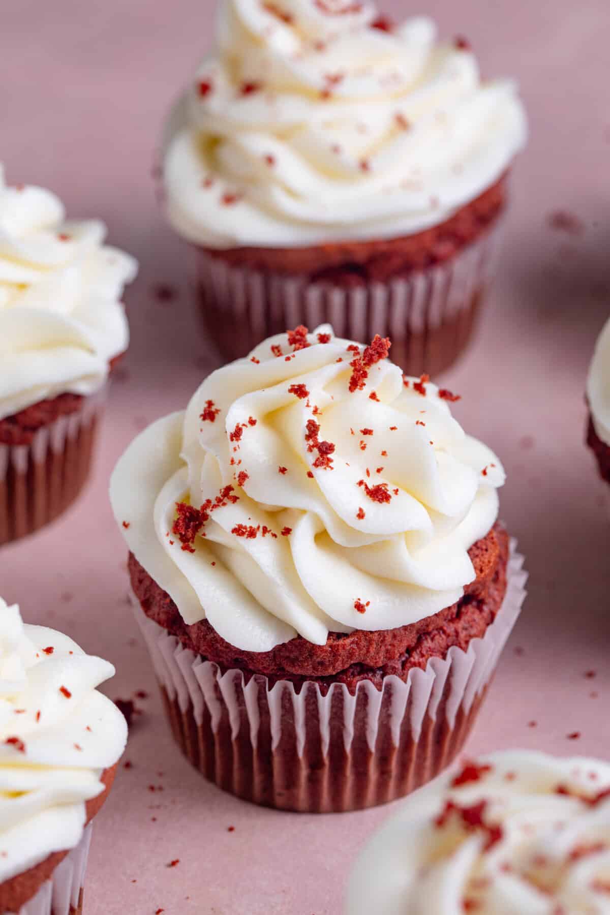 Gluten free red velvet cupcakes with cream cheese frosting on a pink backdrop.