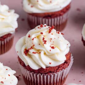 Gluten free red velvet cupcakes with cream cheese frosting on a pink backdrop.