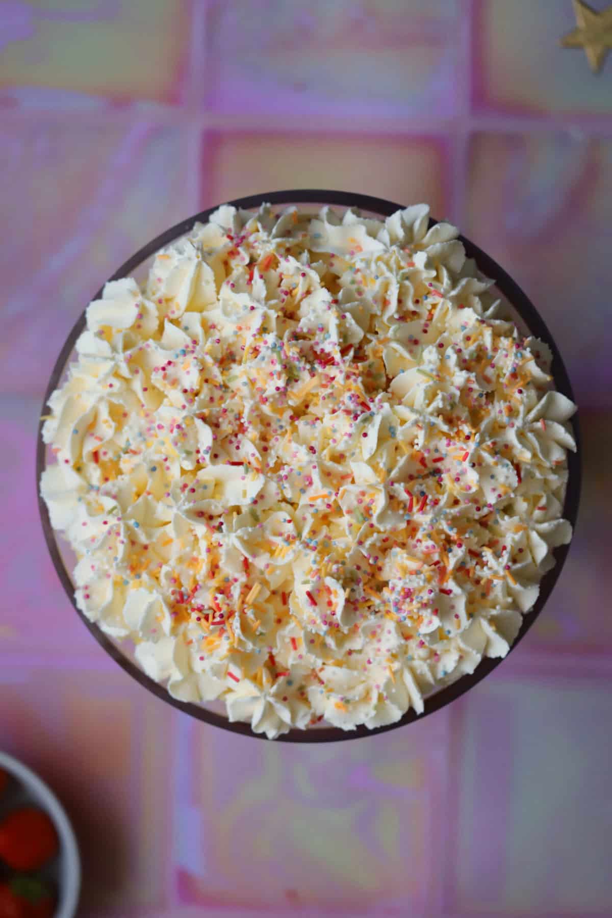 Process shot of a gluten free trifle recipe showing the cream piped onto the trifle and sprinkles on top.