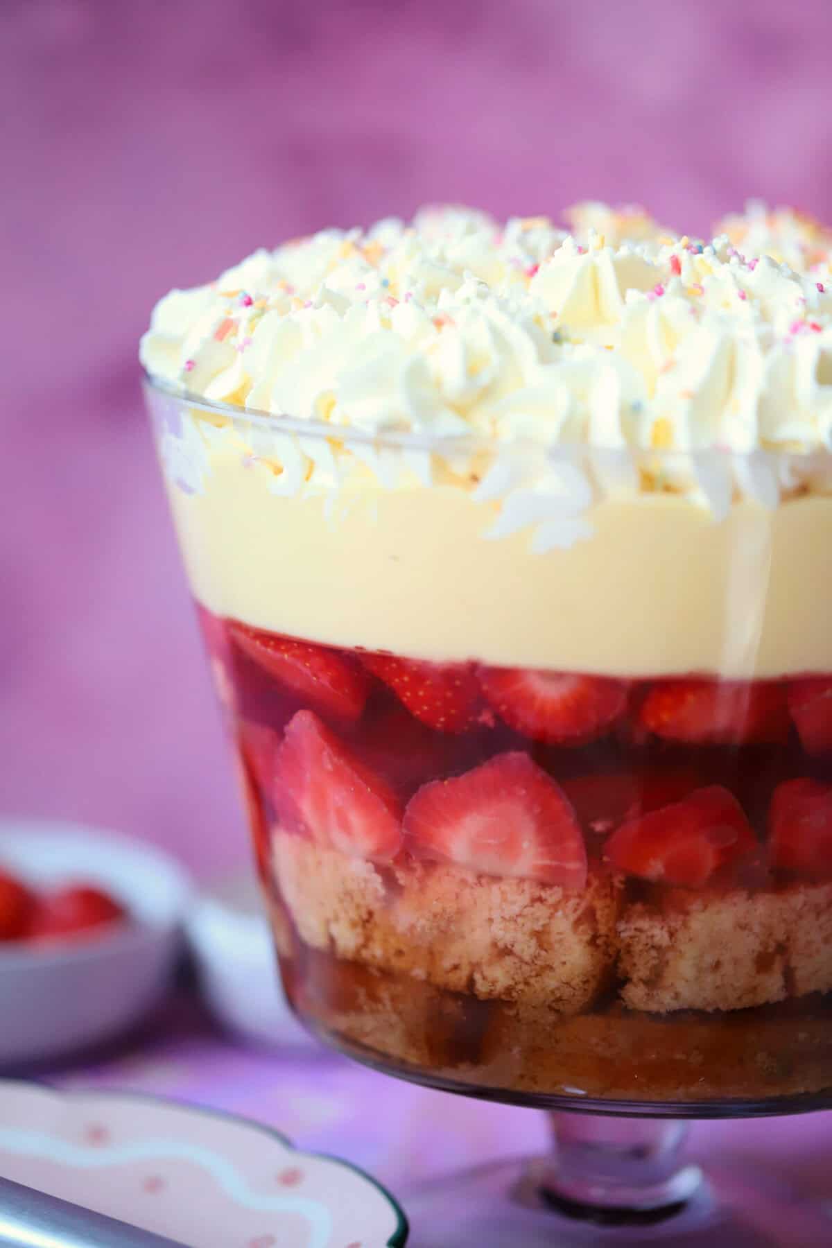 A close up of a gluten free trifle with layers of sponge, fruit, jelly, custard and cream.