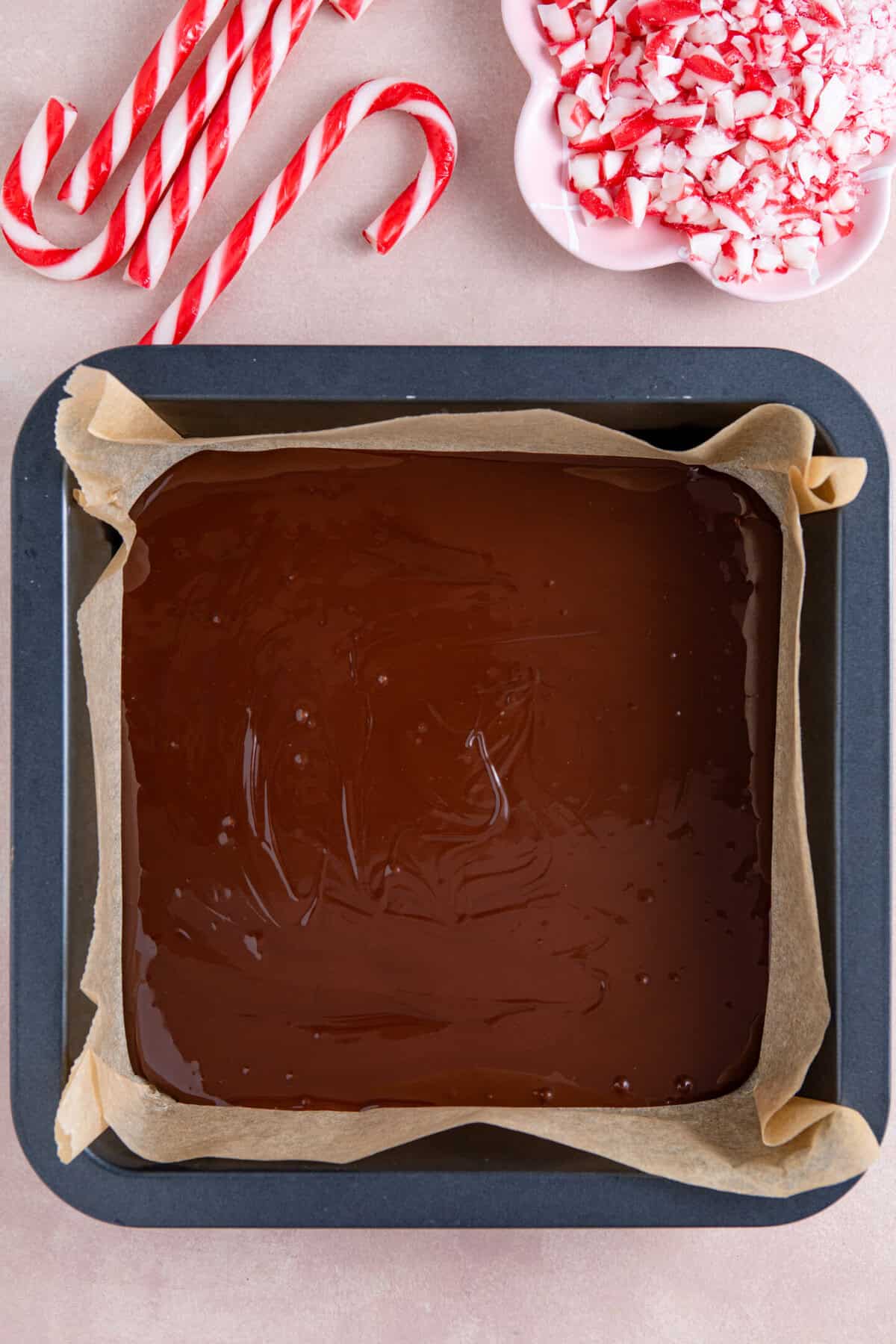 A process shot of peppermint bark recipe showing melted dark chocolate in a lined baking tin.