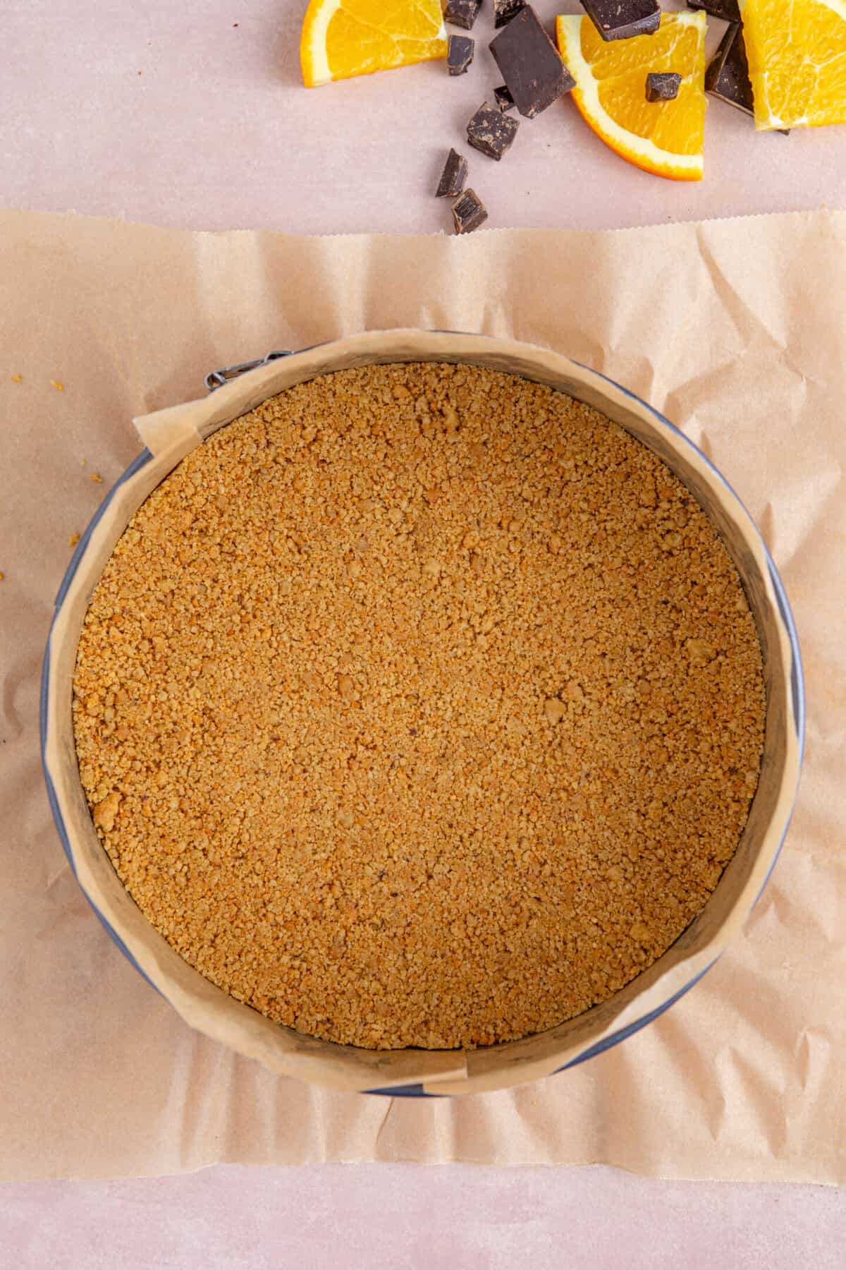 Process shot of a chocolate orange cheesecake recipe showing the biscuit base pressed into a lined tin.