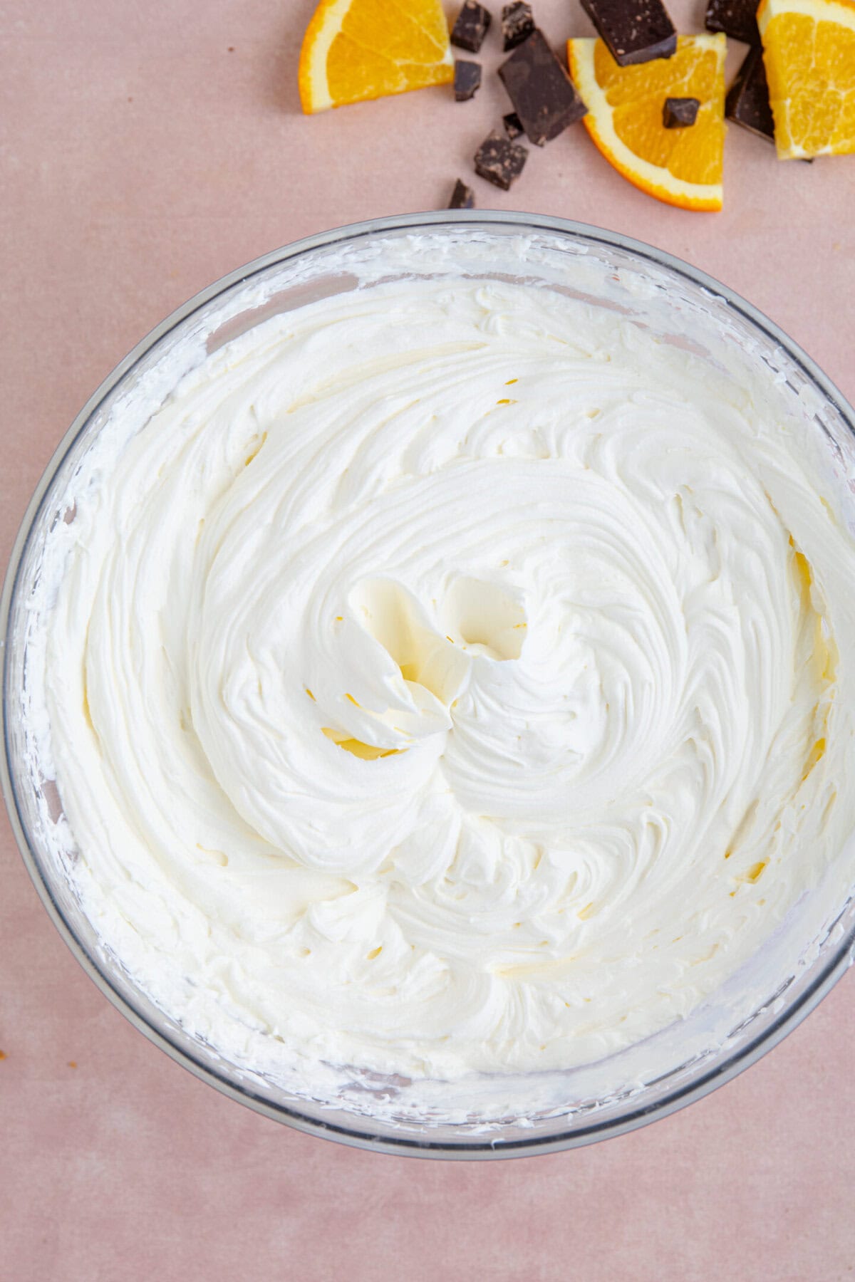 Process shot of a chocolate orange cheesecake recipe showing the whipped cream, cream cheese and icing sugar in a bowl.