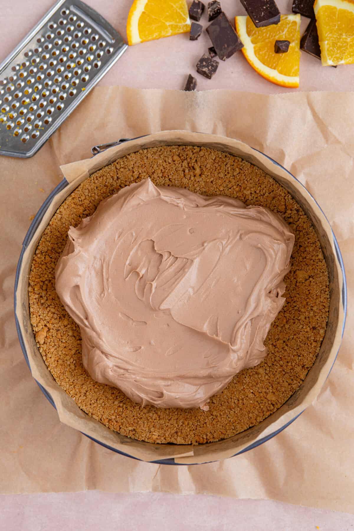 Process shot of a chocolate orange cheesecake recipe showing the cheesecake topping being placed on top of the biscuit base.