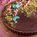 A no bake, gluten free chocolate tart decorated with crushed pistachios, candy canes and edible holly.