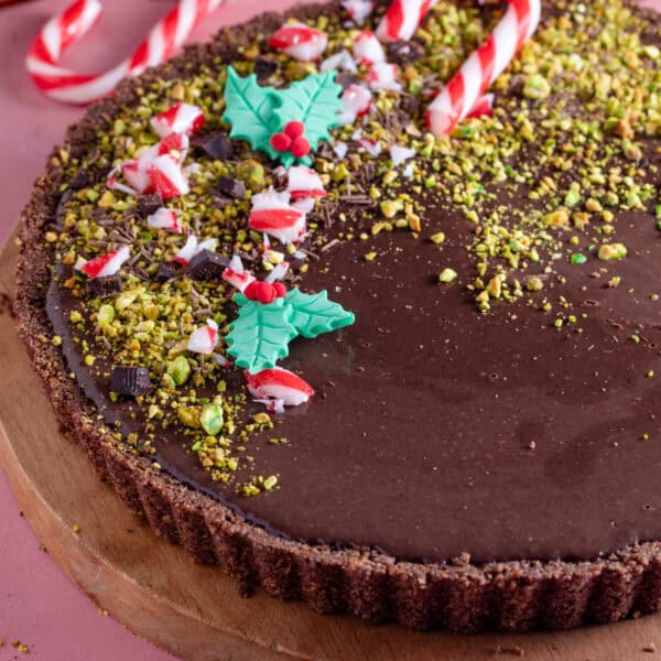 A no bake, gluten free chocolate tart decorated with crushed pistachios, candy canes and edible holly.