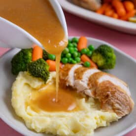 A jug of gluten free gravy being poured over roast chicken and mashed potatoes.