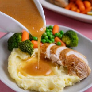 A jug of gluten free gravy being poured over roast chicken and mashed potatoes.