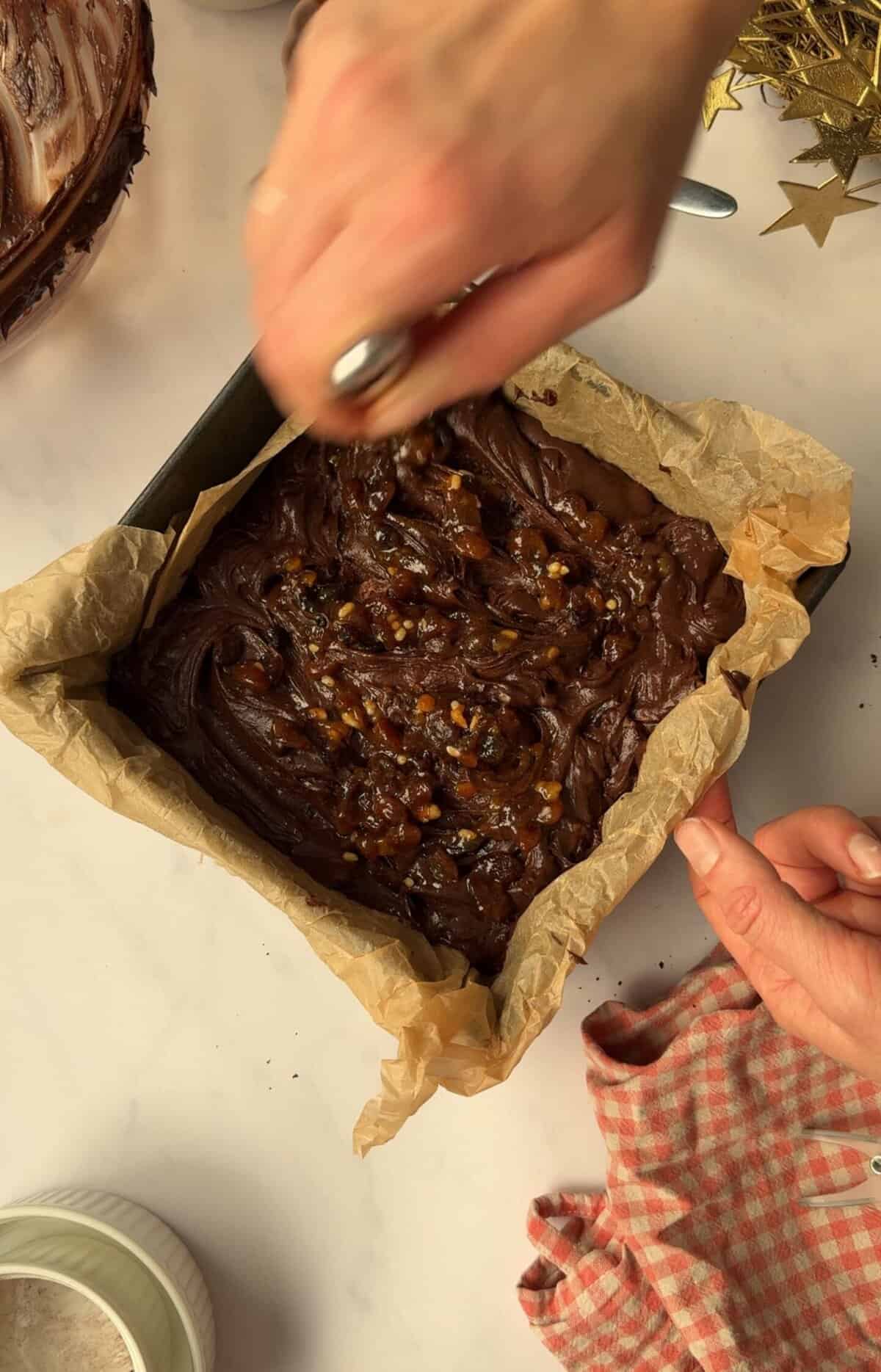 Process shot of mince pie brownies recipe showing a hand swirling mincemeat into a tin of brownie batter using a knife.