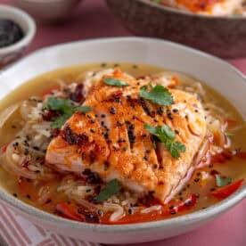 A bowl of brothy rice with salmon on top, garnished with coriander and chilli oil.