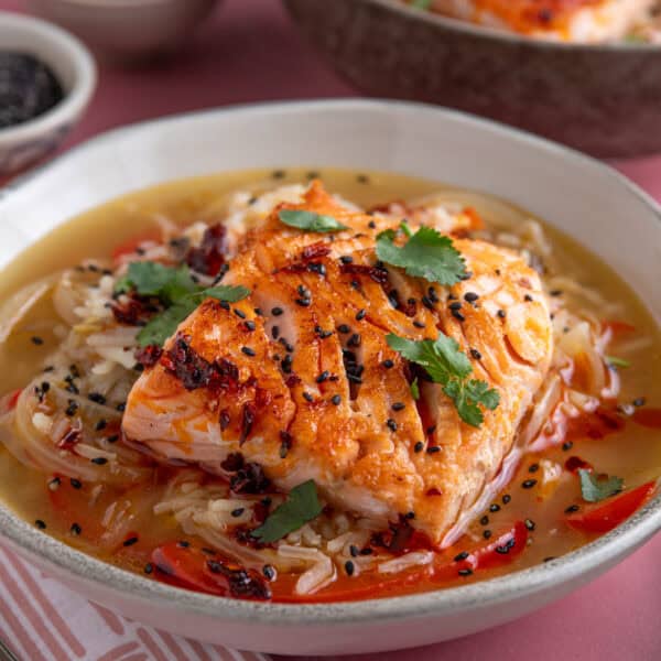 A bowl of brothy rice with salmon on top, garnished with coriander and chilli oil.