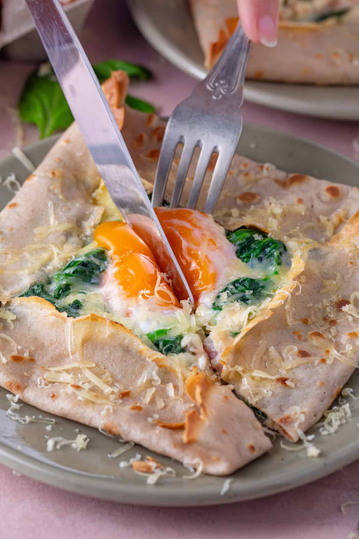 Knife and fork cutting into an egg in the centre of a buckwheat galette.