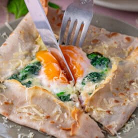 Knife and fork cutting into an egg in the centre of a buckwheat galette.