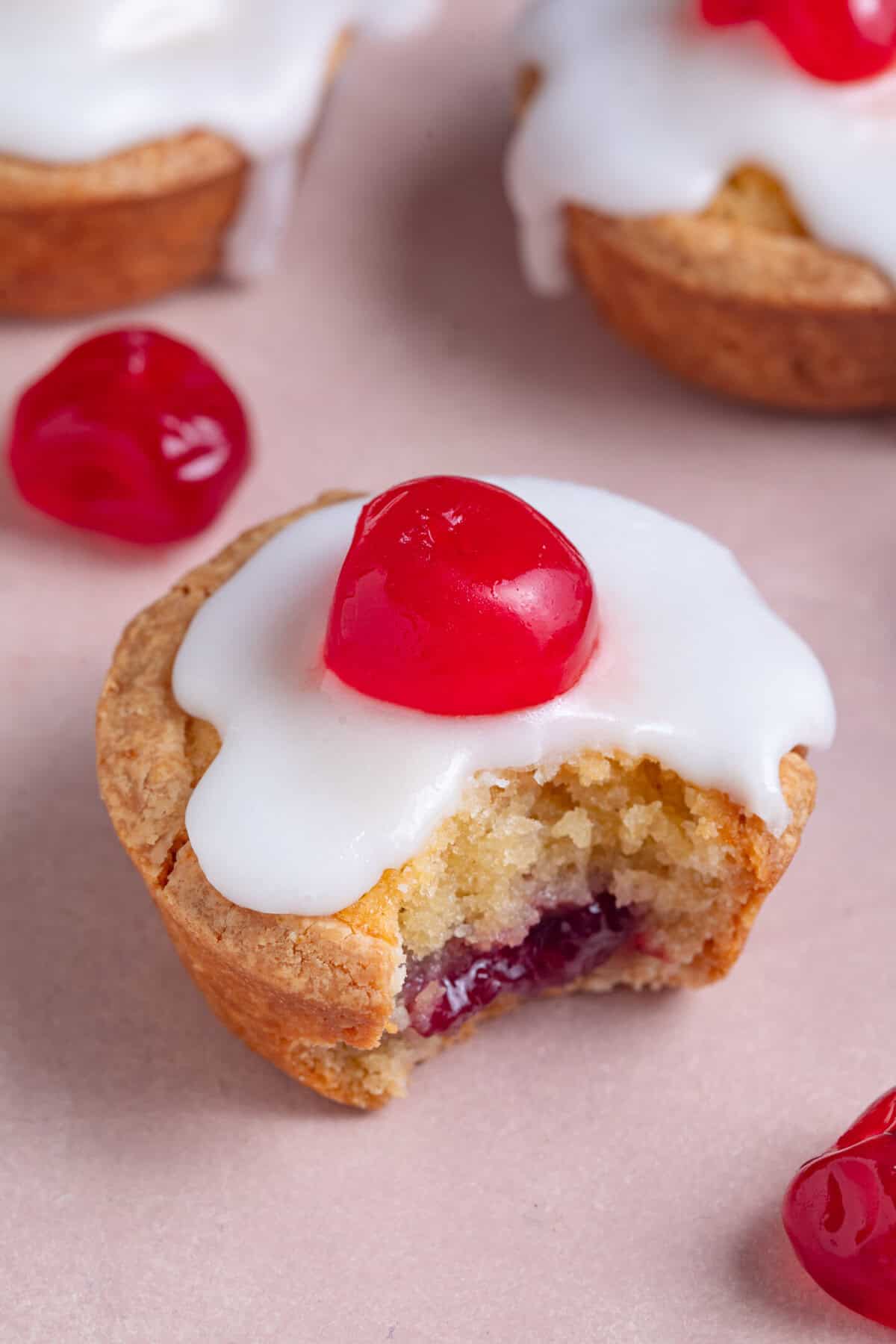 A close up of a gluten free cherry bakewell tart with a bite taken out, showing the jam filling.