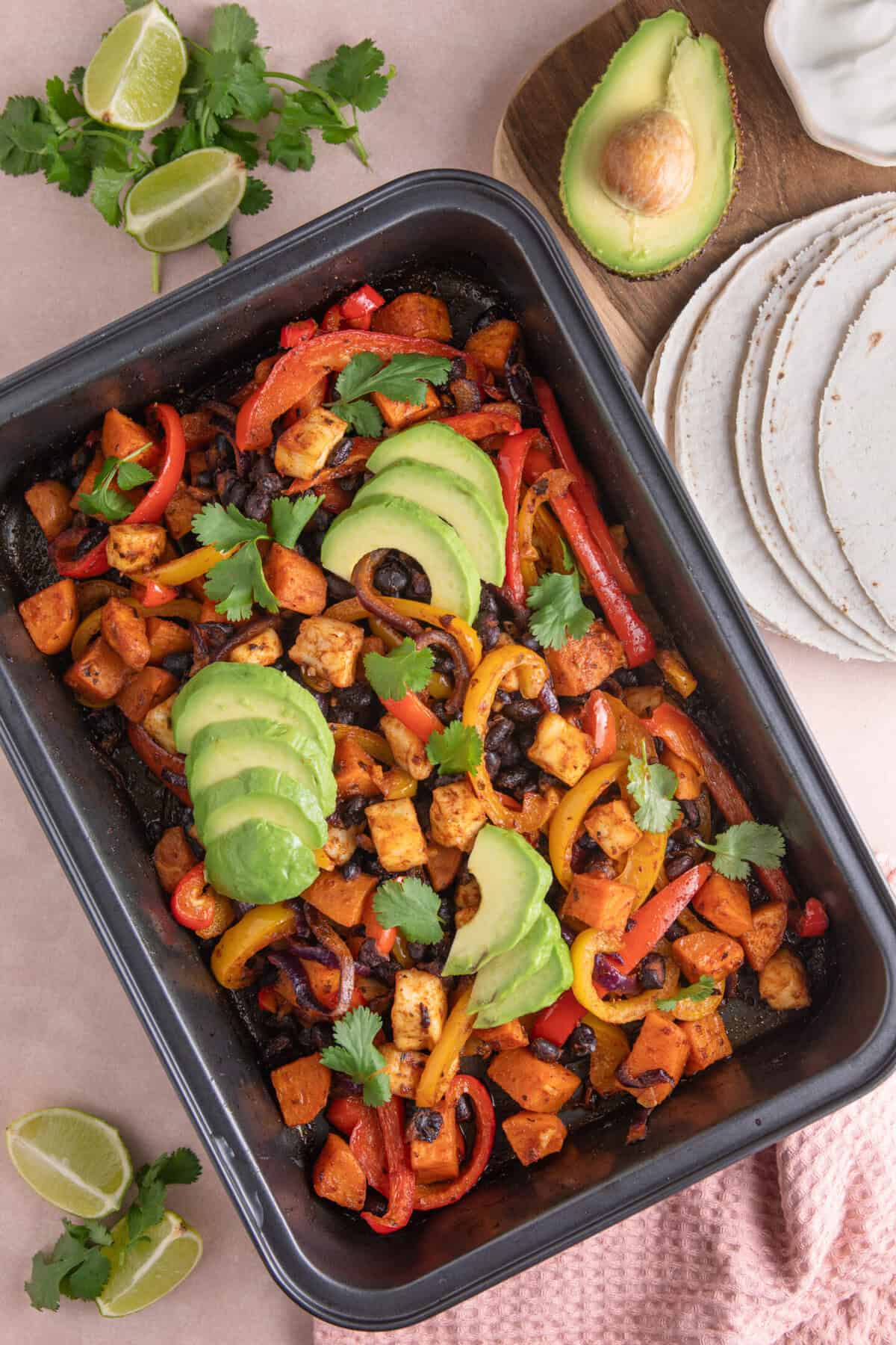 Overhead shot of halloumi taco fillings in a baking tray, with sweet potato, black beans and peppers.