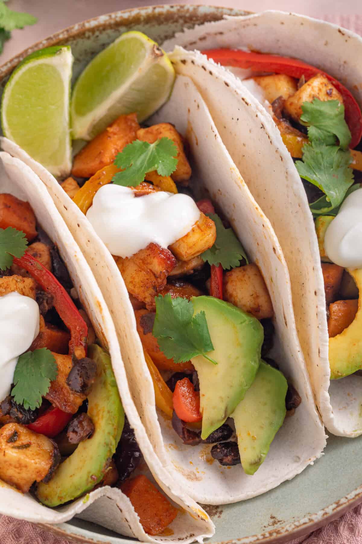 A plate of 3 tacos filled with spicy halloumi and black beans, with avocado and soured cream.