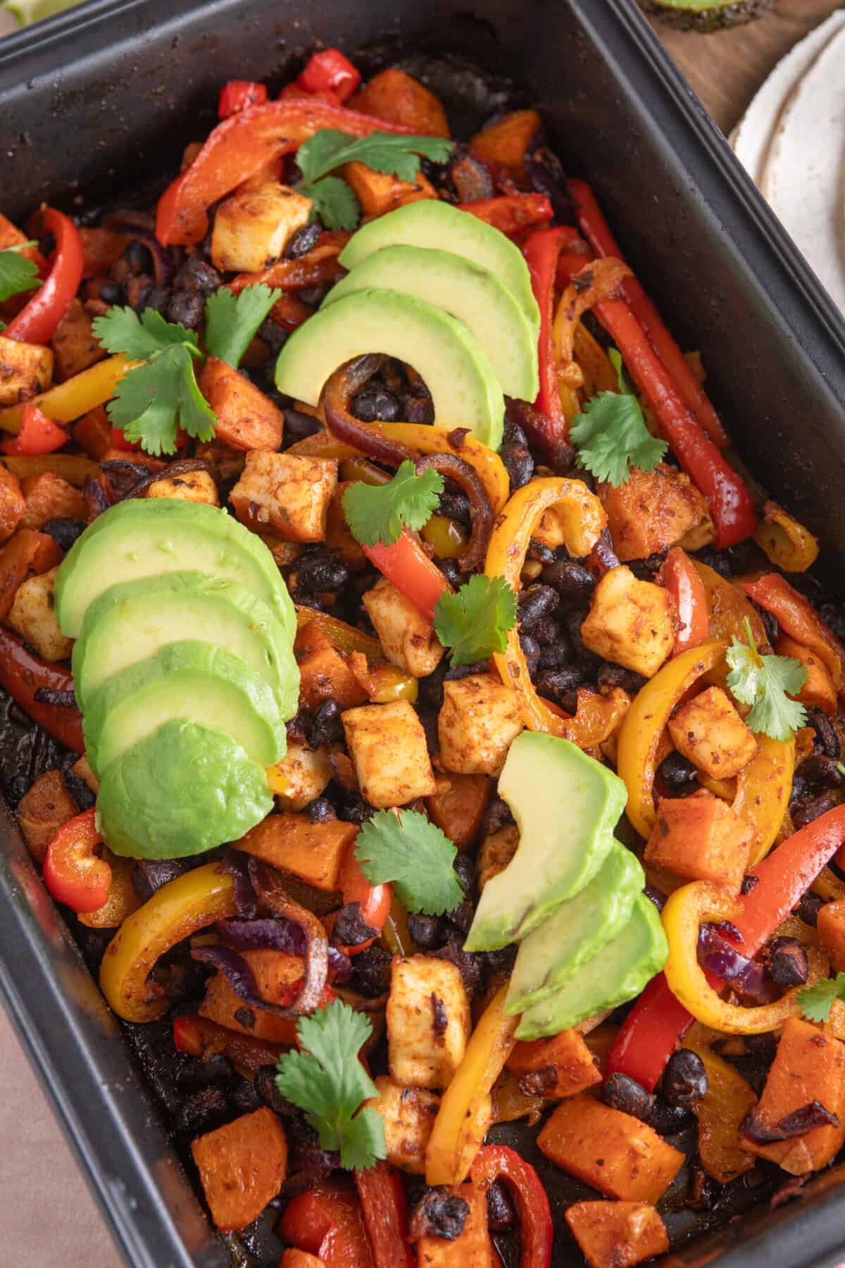 Overhead shot of halloumi taco fillings in a baking tray, with sweet potato, black beans and peppers.