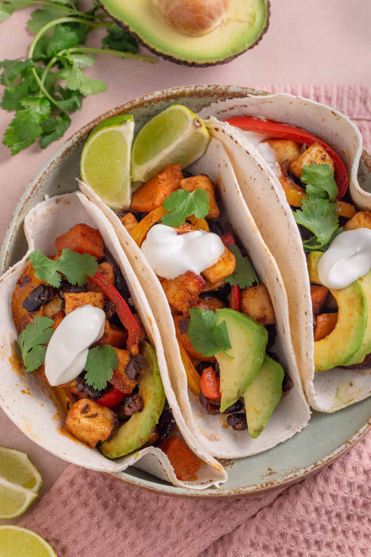 A plate of 3 tacos filled with spicy halloumi and black beans, with avocado and soured cream.