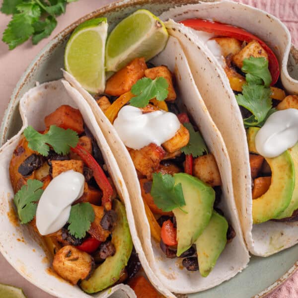 A plate of 3 tacos filled with spicy halloumi and black beans, with avocado and soured cream.