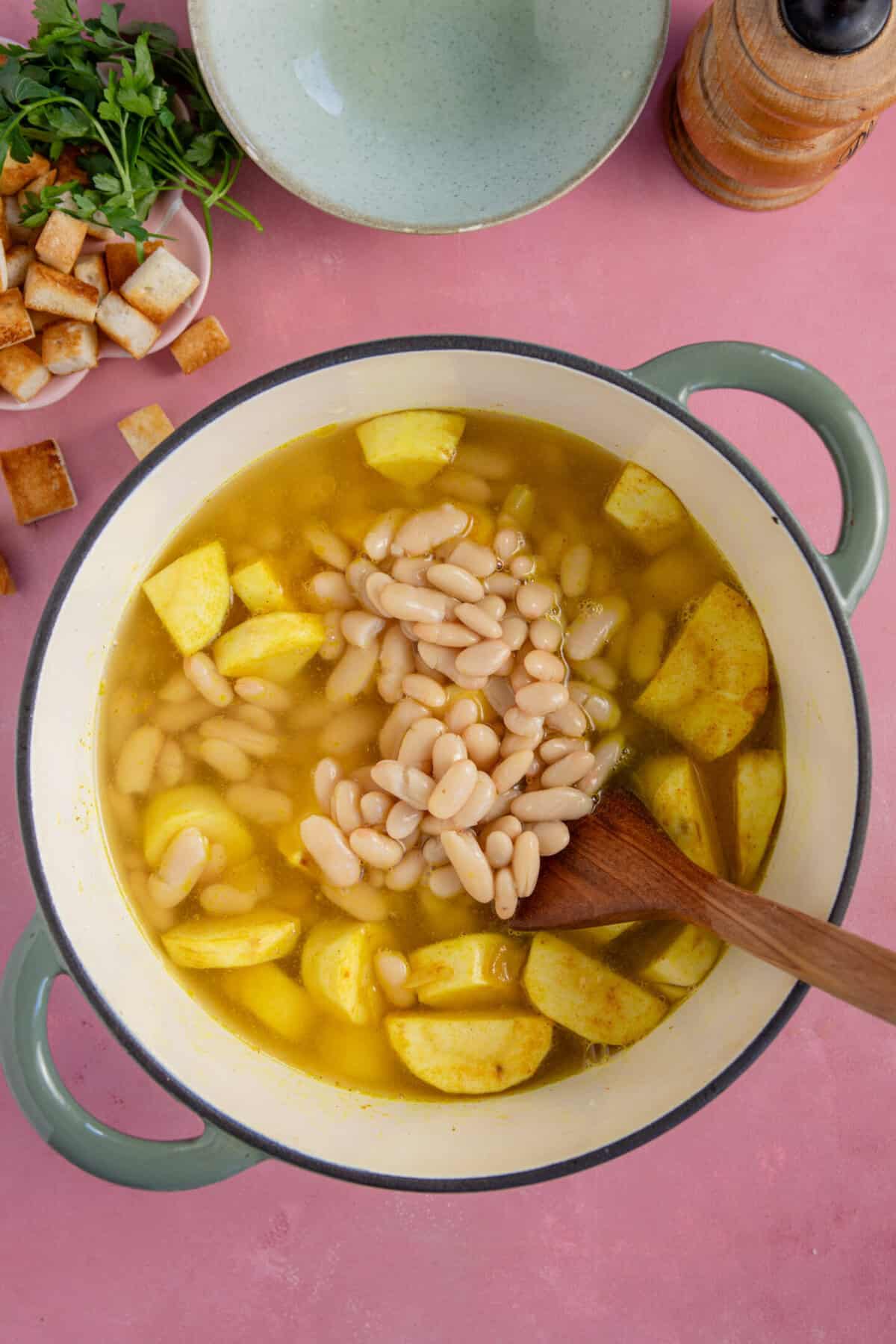 Process shots of parsnip soup recipe showing the stock and cannellini beans added to the pan.