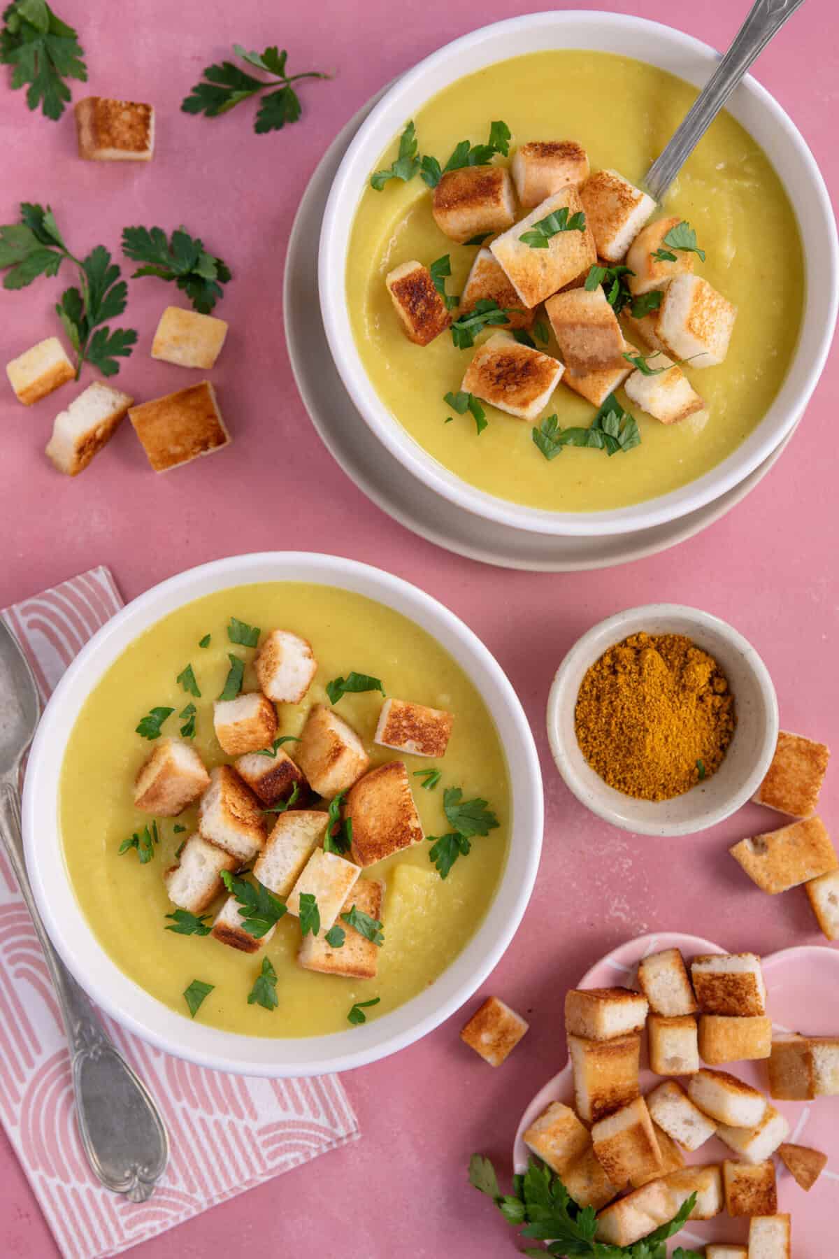 Two bowls of gluten free parsnip soup with croutons and fresh parsley on top.