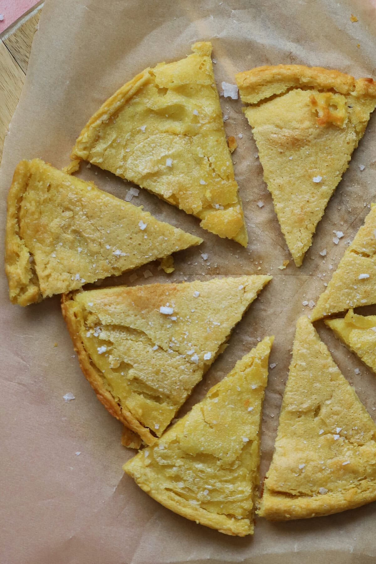 Triangle slices of gluten free socca (chickpea flatbread) on a piece of baking paper.
